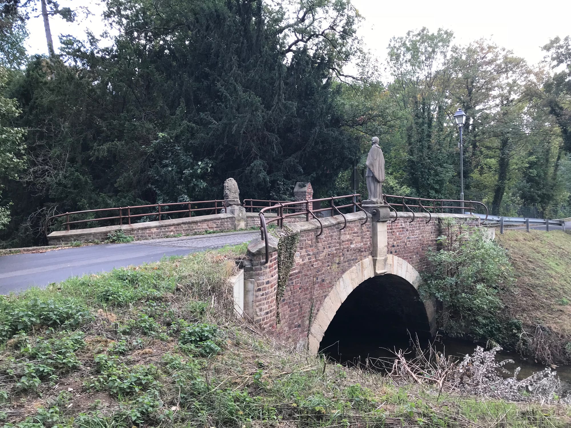 Historic brick bridge over a stream in a wooded park area of Gymnich